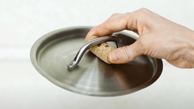 Fingers holding either side of a cork that's been slipped under a pot handle.