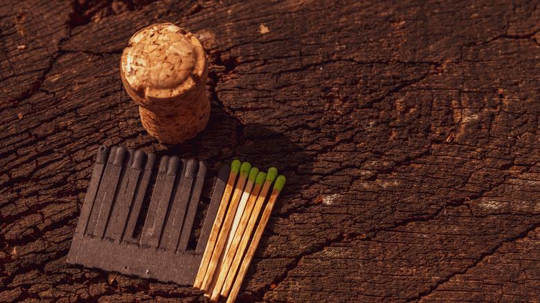 A cork sitting on a wood surface with matches nearby.
