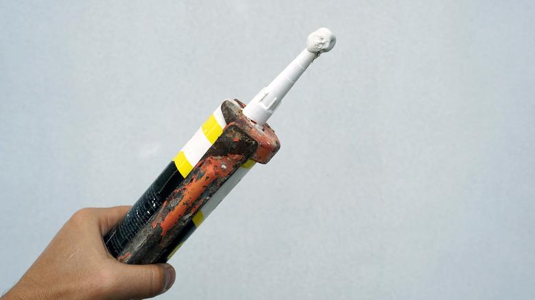 person holding caulk gun against a grey wall