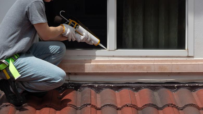 man caulking exterior second floor window on top of roof