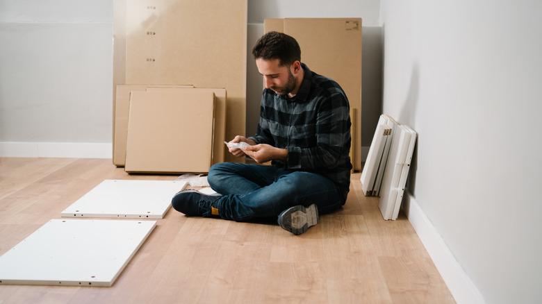 Man sitting on the ground as he puts together an IKEA furniture piece.