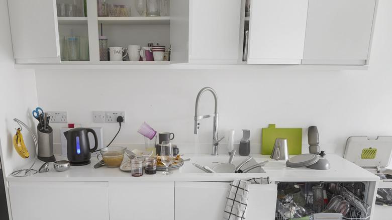 Cluttered kitchen counter with bowls, utensils, cleaning supplies, pots, pans everywhere