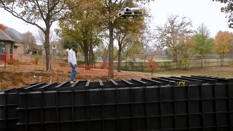 man standing on top of black underground bunker being installed