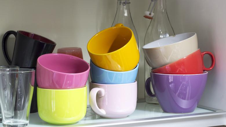 a bunch of stacked colorful coffee mugs in a cabinet