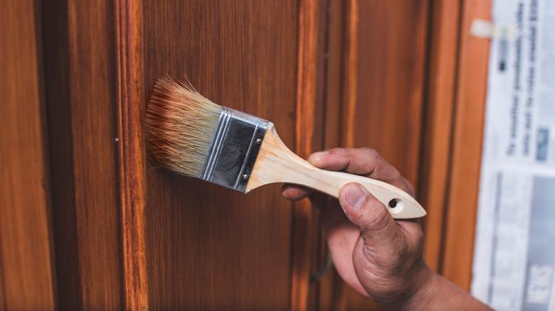 A hand placing varnish on a cabinet door