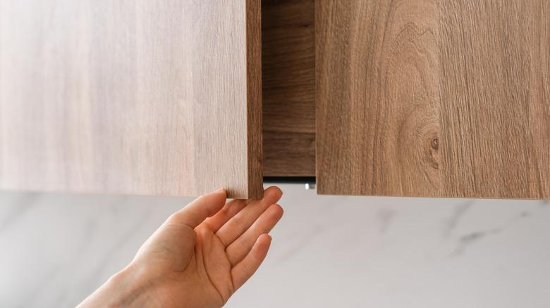 A hand opening a flat cabinet door