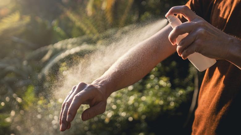 Person spraying repellent on their arm while outdoors