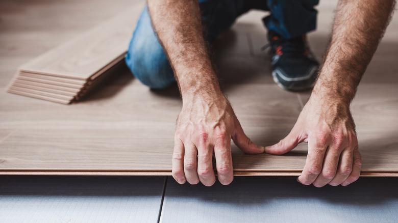 Close-up of male hands placing click-lock flooring over tiles