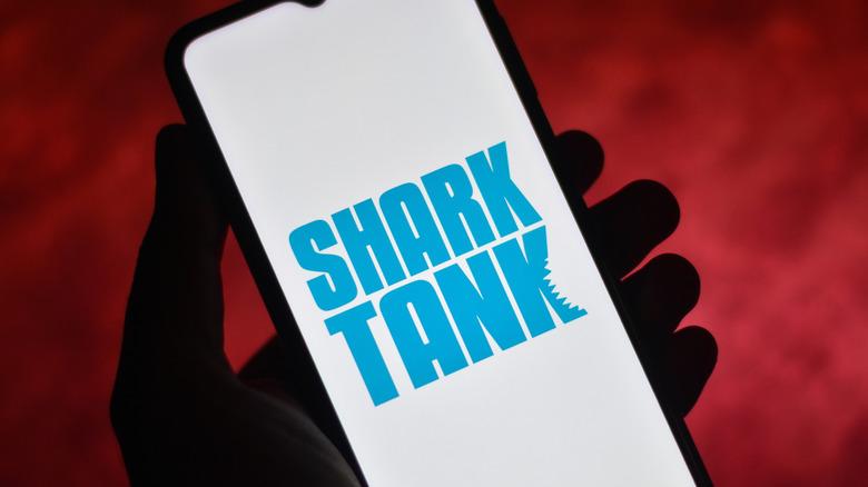 an image of the Shark Tank tv show logo on a mobile phone held in someone's hand with a red background