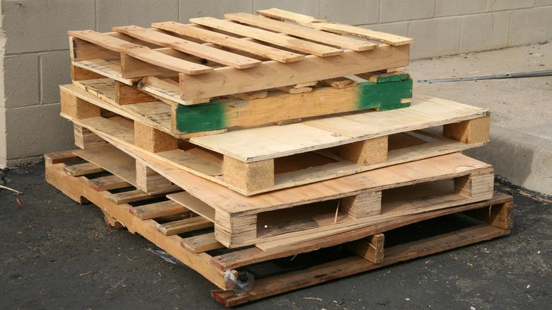 wood pallets stacked on the asphalt ground against a wall beside a sidewalk