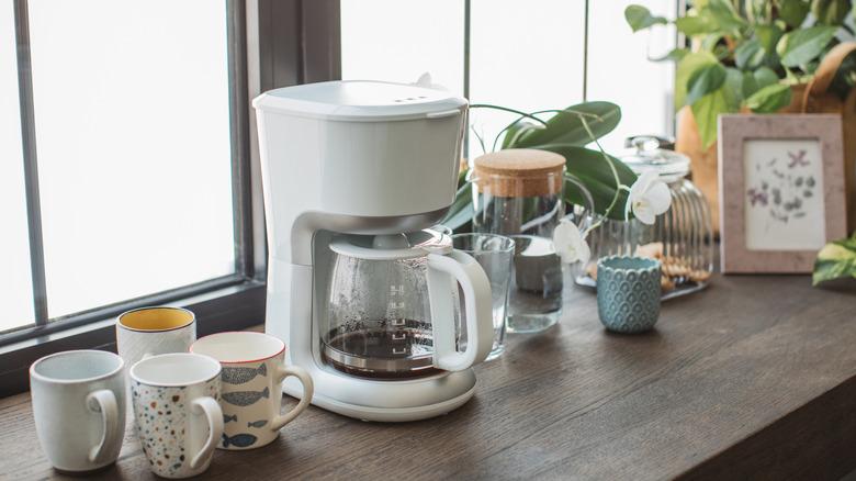 A drip coffee machine on a windowstill with coffee mugs and glass water pitcher