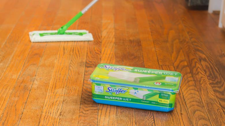 A Swiffer mop and cleaning supplies stand ready to clean a floor.