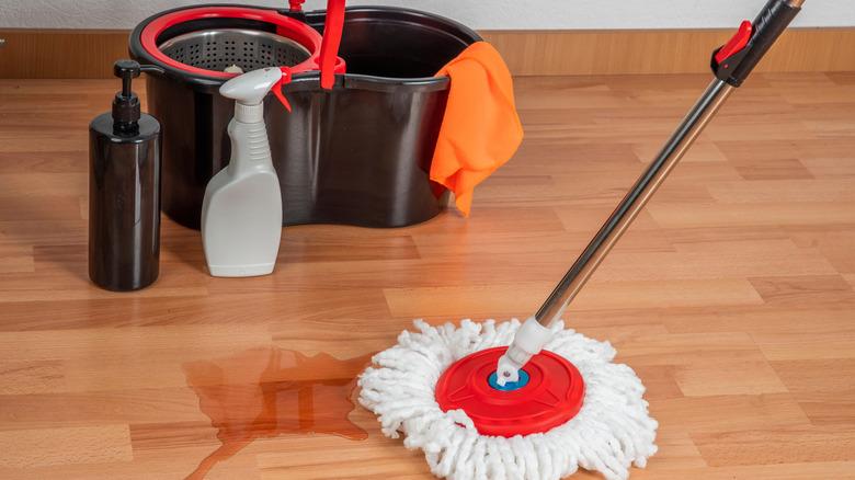 A spin mop and cleaning solutions clean a wood floor.