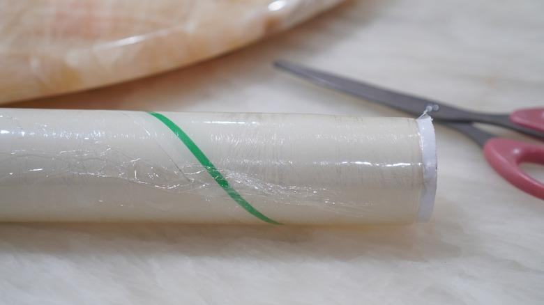 a roll of plastic wrap with scissors in the background