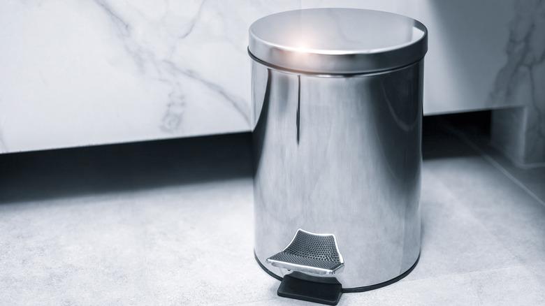 stainless steel step pedal bathroom trash can against marble fixture on white floor